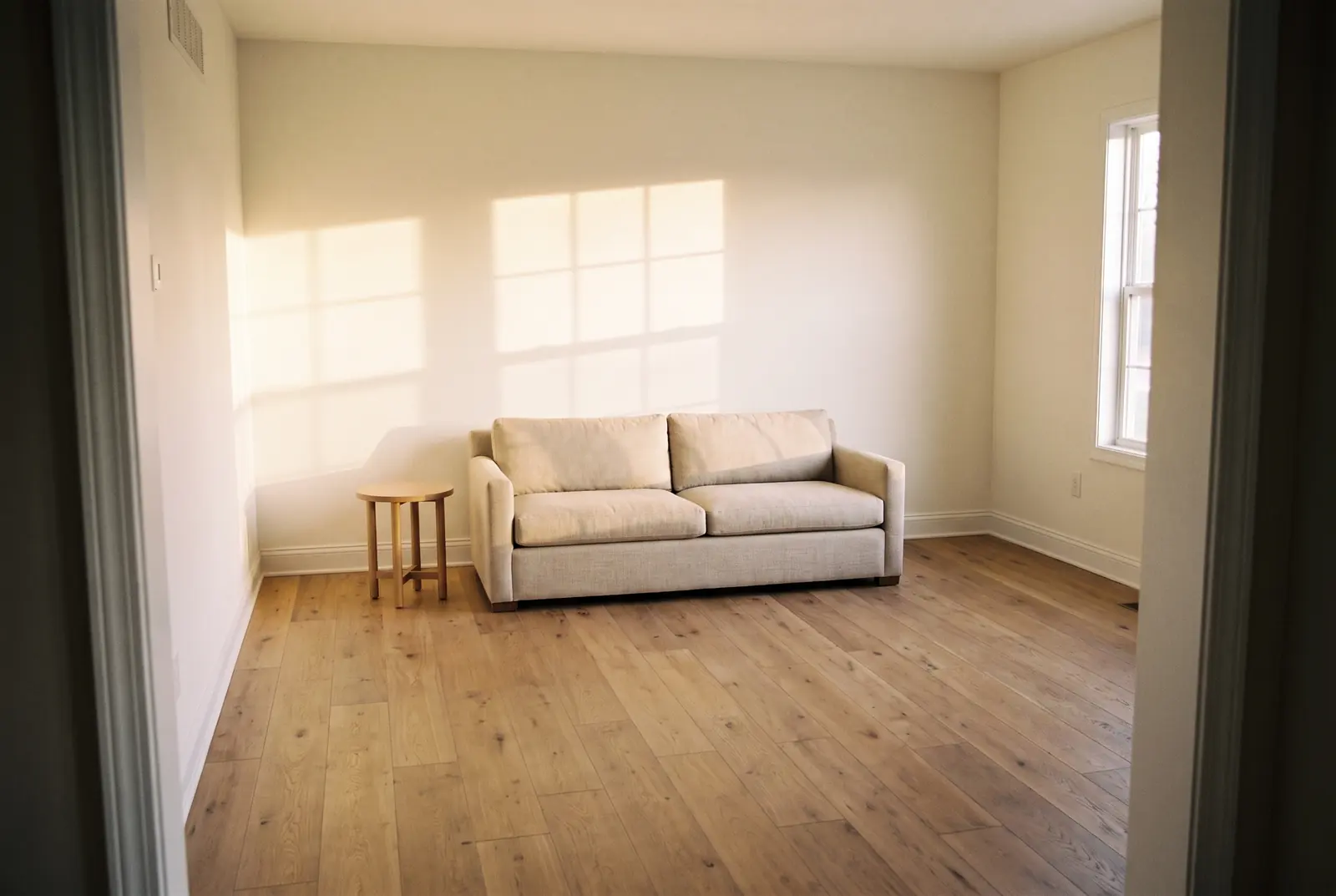 After: the same living room fully rebuilt with new drywall, paint, baseboards, and oak flooring